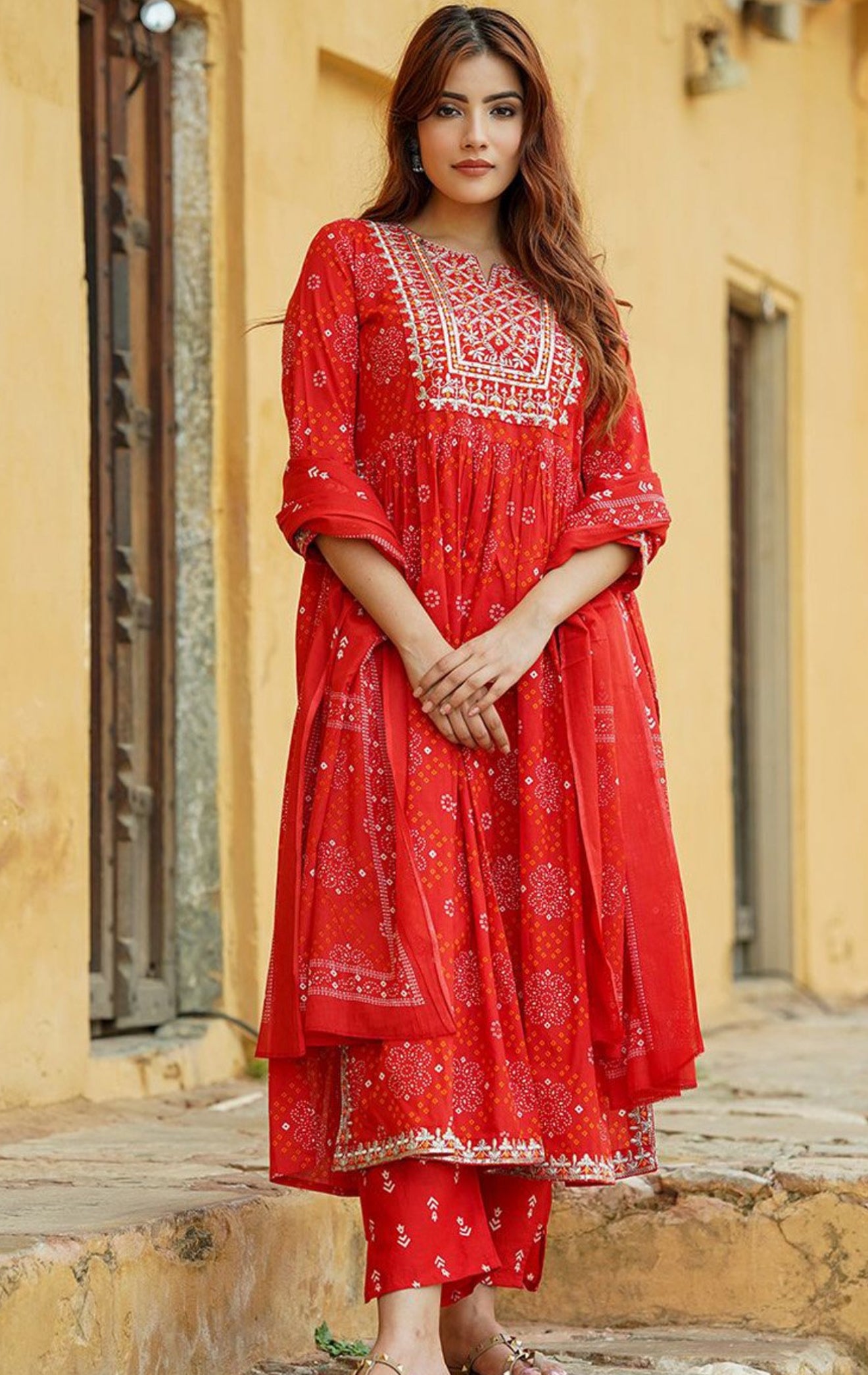 Woman wearing a red traditional outfit with white patterns against a yellow wall.