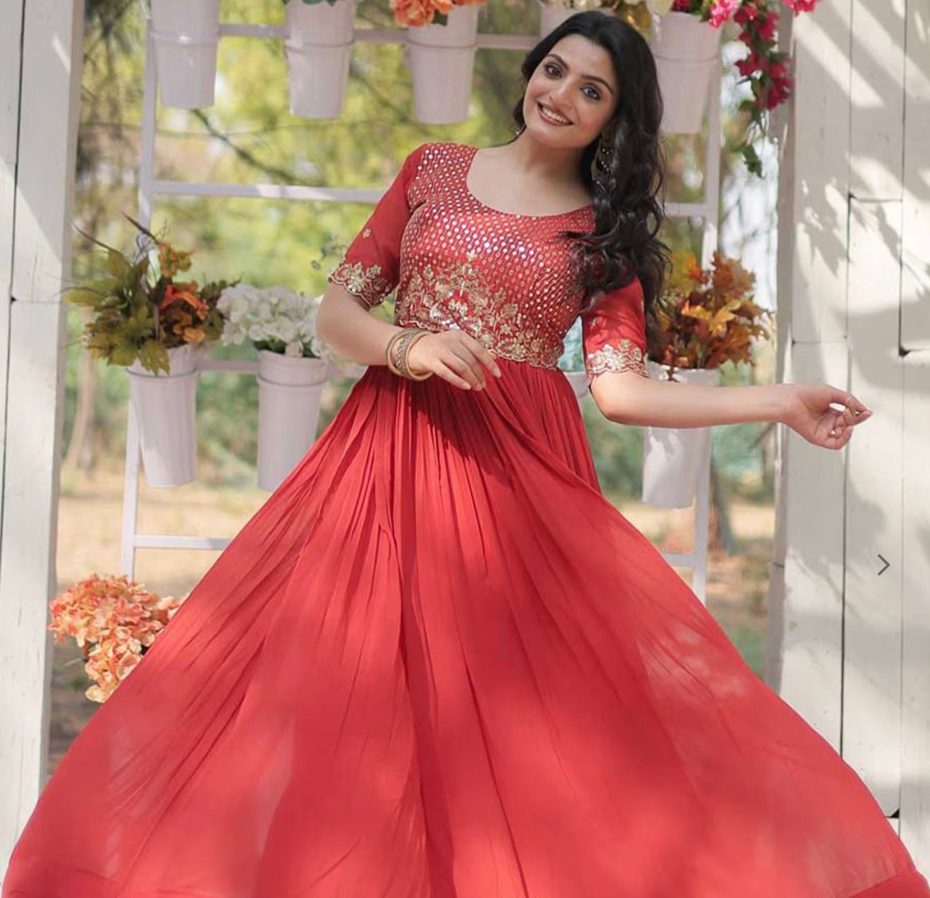 Woman in a red dress with floral decorations standing outdoors.