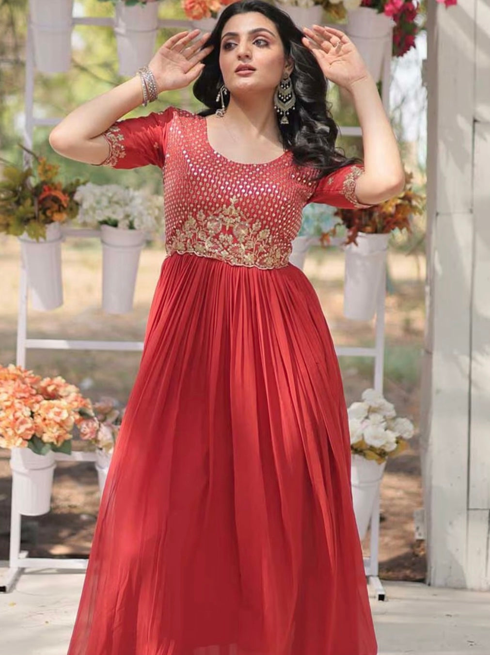 Woman in a red dress with floral patterns standing outdoors with flowers and chairs in the background