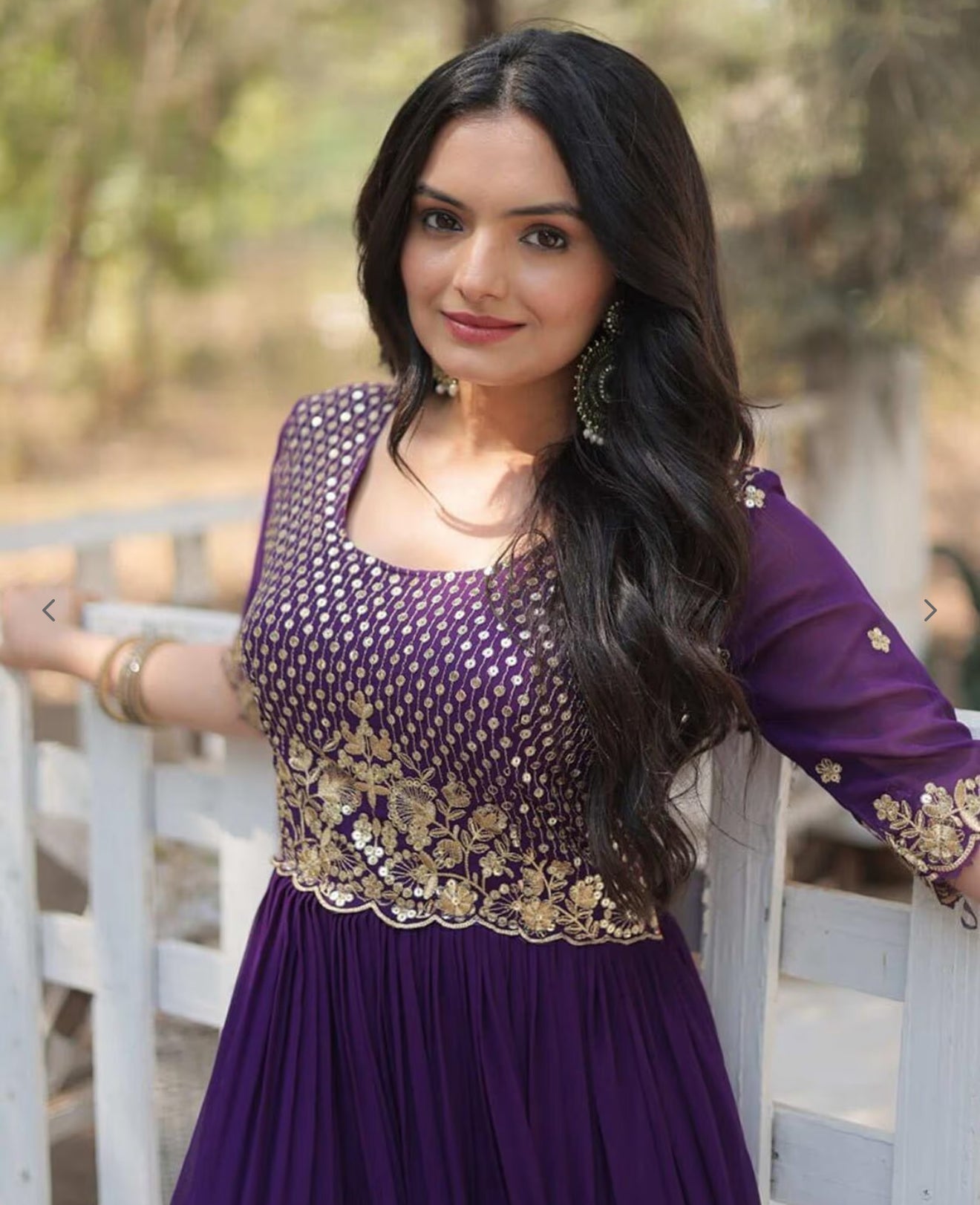 Woman wearing a purple dress with gold embroidery standing outdoors.